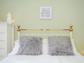 A bedroom with a bed with white sheets and two grey furry pillows a white chest of drawers with a lighthouse decoration and a framed picture on the wall at Quay House in Charlestown