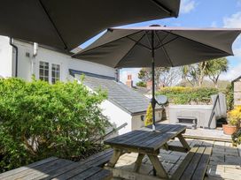 An outdoor patio with wooden picnic tables and umbrellas next to a white house and greenery at Quay House in Charlestown