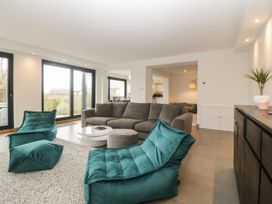 A living room with a gray sofa teal lounge chairs white round coffee tables and large windows at 2 White Rock Court in Paignton
