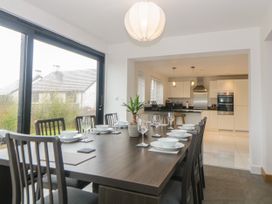A dining area with a large table set with bowls and wine glasses and an open kitchen with white cabinetry at 2 White Rock Court in Paignton