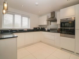 A kitchen with white cabinets black countertops built in oven stovetop and a window with blinds at 2 White Rock Court Paignton