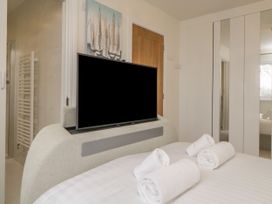 A bedroom with a bed rolled towels a television on a curved stand a wooden door and mirrored wardrobe at 2 White Rock Court in Paignton