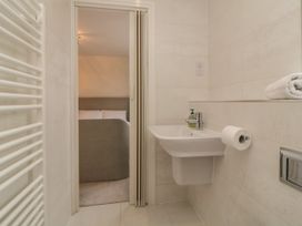 A bathroom with a sink, soap dispenser, toilet paper, towel, and a view into a bedroom with a bed at 2 White Rock Court in Paignton