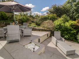 An outdoor patio with a table and chairs under an umbrella and a lounge chair surrounded by plants at 2 White Rock Court in Paignton
