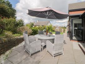 An outdoor patio with a round glass table surrounded by six woven chairs and a large umbrella at 2 White Rock Court in Paignton