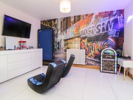 A gaming room with two chairs a wall-mounted TV a white cabinet a jukebox and graffiti wall art at 2 White Rock Court in Paignton