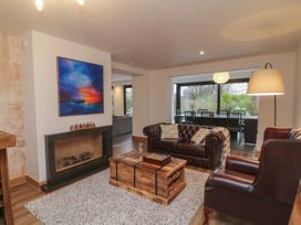 A living room with a fireplace a leather sofa a wooden coffee table and a dining area with black chairs and large windows at 2 White Rock Court Paignton