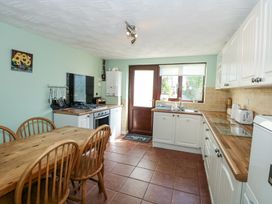 A kitchen with a wooden table and chairs a gas stove a sink under a window and white cabinets at Cuddfan in Tremadog