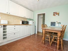 A kitchen with white cabinets a wooden dining table with four chairs and appliances at Cuddfan in Tremadog
