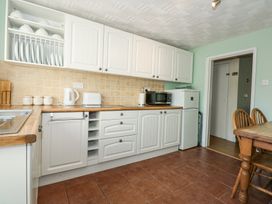 A kitchen with white cabinets wooden countertops a microwave toaster kettle and a dining table with chairs at Cuddfan in Tremadog