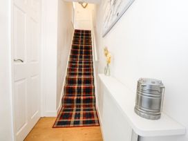 A hallway with a staircase covered in plaid carpet a white door on the left and a shelf with a vase and a silver lantern at Cuddfan in Tremadog