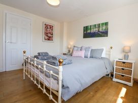 A bedroom with a bed covered in gray bedding towels on the bed two bedside tables with lamps wooden floor and two paintings on the walls at Cuddfan in Tremadog