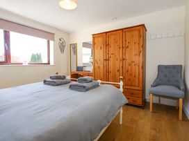A bedroom with a bed covered in gray linens and towels a wooden wardrobe a dressing table with a mirror and a gray chair at Cuddfan in Tremadog