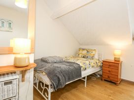 A bedroom with a single bed covered with a yellow patterned duvet and gray blanket next to a wooden bedside table with a lamp and a mirror on the wall at Cuddfan in Tremadog