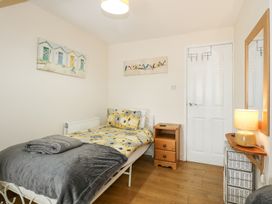 A bedroom with a single bed with yellow and grey bedding a wooden nightstand a white door a wicker drawer unit and two paintings on the wall at Cuddfan in Tremadog