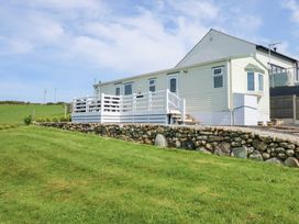 An exterior view of a single-story caravan with a white deck and stone retaining wall on a grassy landscape at Ty Newydd Caravan in Llannor near Pwllheli