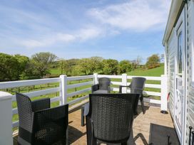An outdoor deck with four black chairs and a white railing overlooking green fields and trees at Ty Newydd Caravan in Llannor near Pwllheli