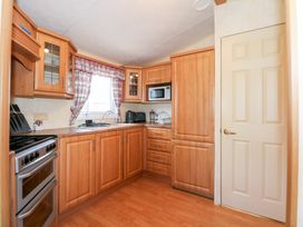 A kitchen with wooden cabinets a stove a microwave a sink and appliances at Ty Newydd Caravan in Llannor near Pwllheli