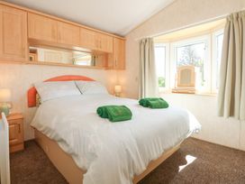 A bedroom with a bed under cupboards and a bay window with curtains at Ty Newydd Caravan in Llannor near Pwllheli