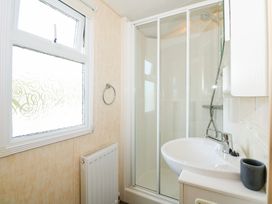 A bathroom with a sink and shower enclosure next to a frosted window and radiator at Ty Newydd Caravan Llannor near Pwllheli
