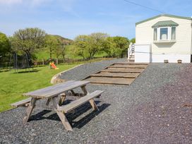 An outdoor area with a wooden picnic table on gravel next to steps leading to a caravan and a grassy area with a trampoline and slide at Ty Newydd Caravan in Llannor near Pwllheli