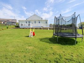 A backyard with a trampoline and a small slide on a grassy lawn at Ty Newydd Caravan in Llannor near Pwllheli