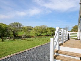 A wooden deck with white railings overlooking a fenced grassy yard with trees and hills in the distance at Ty Newydd Caravan in Llannor near Pwllheli