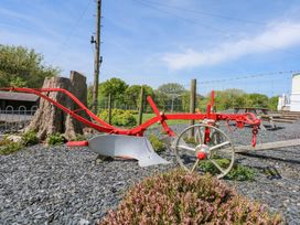 A red and silver farming plow on gravel with a tree stump and fencing in the background at Ty Newydd Caravan in Llannor near Pwllheli
