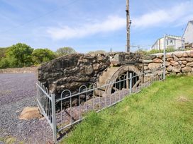 An outdoor stone structure with a water wheel next to a metal fence and grassy area at Ty Newydd Caravan in Llannor near Pwllheli