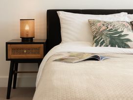A bedroom with a bed, nightstand, lamp, and magazine at Sandy Cove in Praa Sands