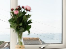 A view of flowers in a vase and the ocean from a window at Sandy Cove in Praa Sands