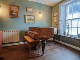 A living room with a piano and framed paintings at The Fernery in Colyton