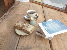 A coffee cup, plate with cake, and books on a wooden table at Betsy's Burrow