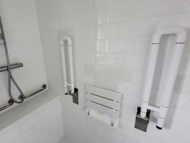 A bathroom with grab bars and a folding bench at Top Of The Lane Luxury Holiday Apartment in Benllech