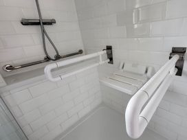 A bathroom with grab bars and a folding shower seat at Top Of The Lane Luxury Holiday Apartment in Benllech