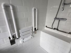 A bathroom with grab bars and a folding shower seat at Top Of The Lane Luxury Holiday Apartment in Benllech