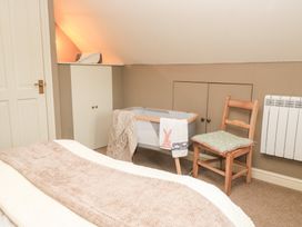 A bedroom with a bed, blanket, cot, chair, and wardrobe at Pudding Hill Barn Cottage in Bibury