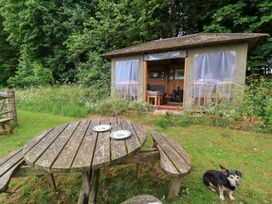 A cabin in a garden with a wooden table and chairs at Pudding Hill Barn Cottage Bibury