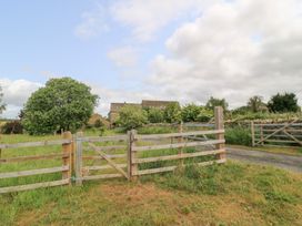 A gate opening to a grassy area with trees and a farmhouse at Pudding Hill Barn Cottage in Bibury