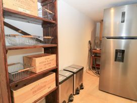 A kitchen with a refrigerator, shelving unit, and trash cans at Pudding Hill Barn Cottage Bibury