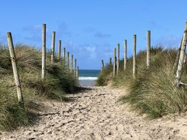 A sandy pathway leading to the beach with grass and wooden posts at Kippy Cottage in Truro