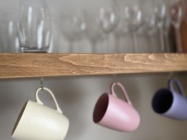 A shelf with glasses and hanging cups at Kippy Cottage in Porthtowan