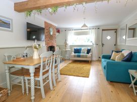 A living room with a dining table and chairs a teal sofa and a beige armchair by a window at Herbies Cottage in Snettisham