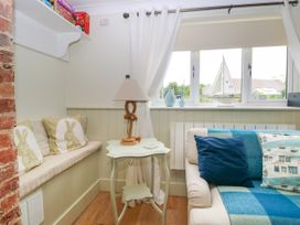 A corner of a living room with a cushioned bench with rabbit pillows a small side table with a lamp and a sofa with blue cushions at Herbies Cottage in Snettisham