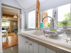 A kitchen sink with sponge and cloth in a rack next to a window and a view into a dining and living area at Herbies Cottage in Snettisham
