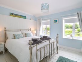 A bedroom with a metal bed frame white bedding blue walls and two windows at Herbies Cottage in Snettisham