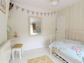 A bedroom with a single bed with floral bedding a small cushioned stool a wall mirror bunting on the wall and a yellow rug at Herbies Cottage in Snettisham
