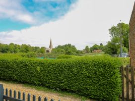 A garden with a dense green hedge and a gravel path with a church steeple and trees in the background at Herbies Cottage in Snettisham