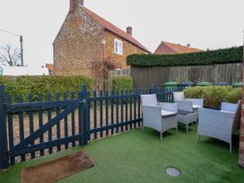 An outdoor patio area with four wicker chairs and a small table on artificial grass near a blue wooden gate at Herbies Cottage in Snettisham
