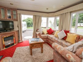 A living area with an L shaped sofa with cushions a small wooden table carpet a fireplace and a television at 2 Old Orchard in Brockton near Much Wenlock